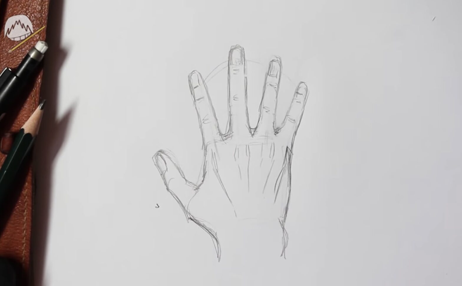 A sketch of an open human hand from the back view, with drawing pens and pencils on a table